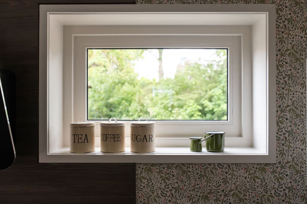 Fensternische mit Tee-, Kaffee- und Zuckerdosen und grünen Emaille-Kännchen