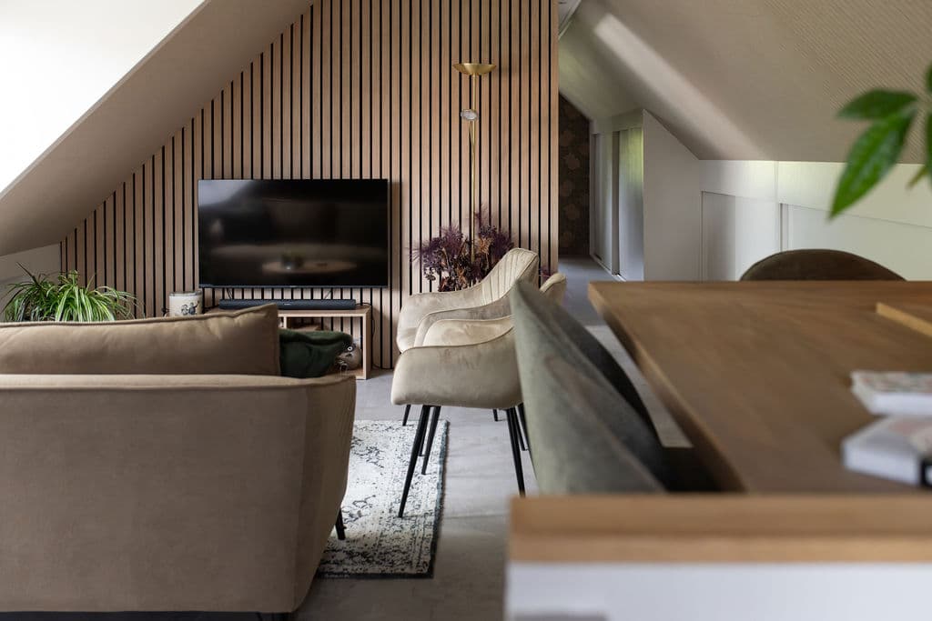 Weite Sitzecke mit Sofa, Sesseln und TV vor Holzlattenwand